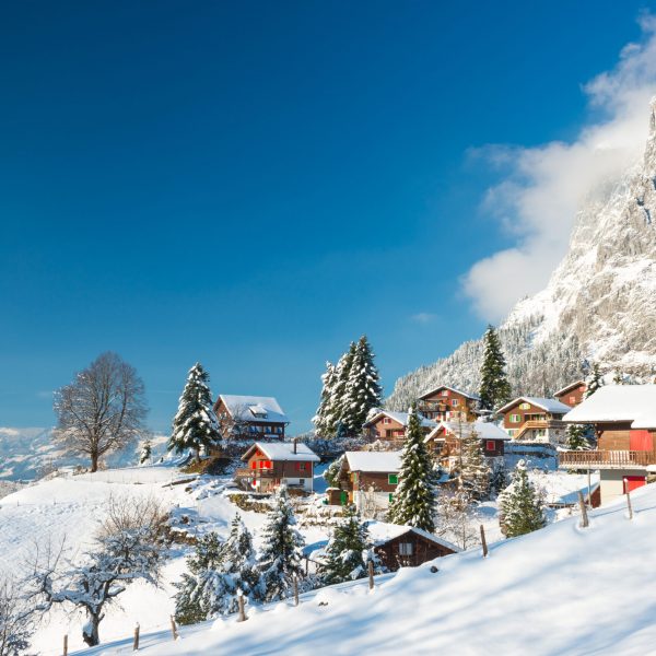 Travel to Switzerland in the winter. Alpine Village in the snow. Traditional houses with red shutters and roofs.